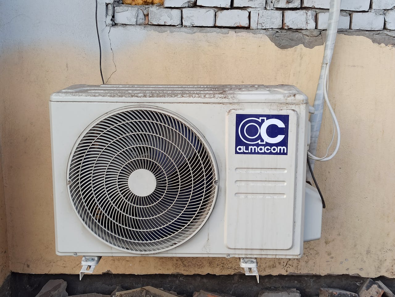 A well-used outdoor air conditioning unit affixed to a brick wall, showcasing urban climate control.